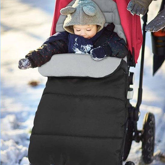Bébé emmitouflé dans une chancelière bébé noire pendant une promenade hivernale dans la neige.