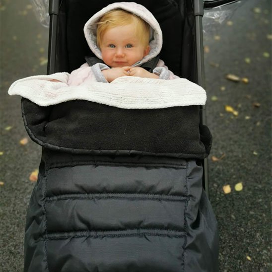 Bébé blond bien emmitouflé dans une chancelière noire douce et chaude pour la saison froide.