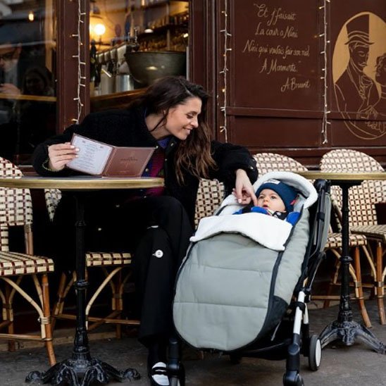 Maman prenant un café pendant que son bébé repose bien au chaud dans une chancelière poussette hiver.