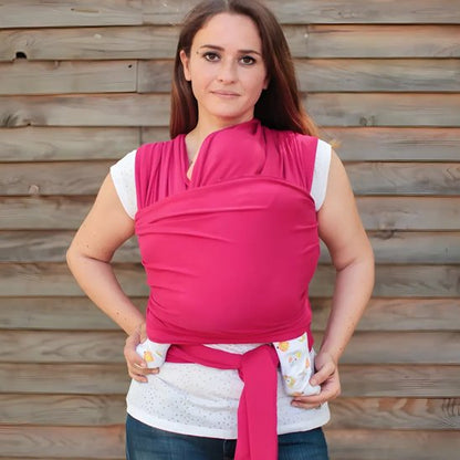 Bébé confortablement installe dans une échappe de portage rose et ergonomique.