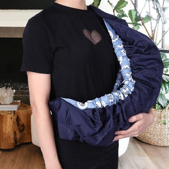 Parent portant une écharpe de portage bébé bleu marine ergonomique et confortable dans un intérieur naturel.