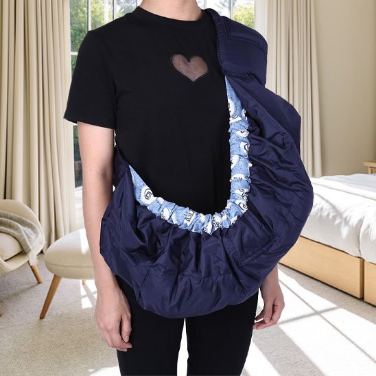 Écharpe de portage-bébé bleu marine ajustable portée sur l'épaule d'un parent dans une chambre lumineuse.