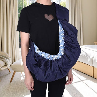 Écharpe de portage-bébé bleu marine ajustable portée sur l'épaule d'un parent dans une chambre lumineuse.