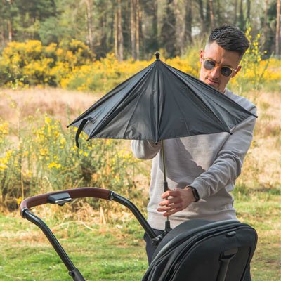 Papa installant une ombrelle sur la poussette pour protéger le bébé du soleil pendant la promenade.