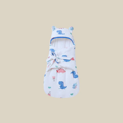Nid d'ange pour bébé à motif dinosaure, avec capuche à oreilles et nœud décoratif sur fond beige.
