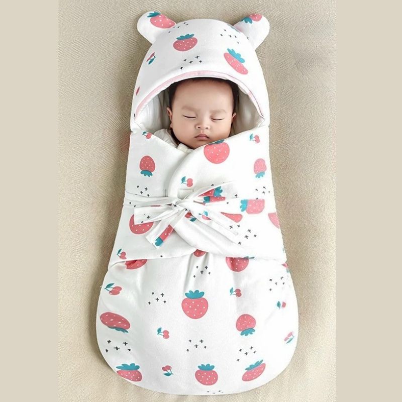 Bébé endormi dans un nid d'ange à motif (fraises) rouge, avec capuche à oreilles et intérieur doux.