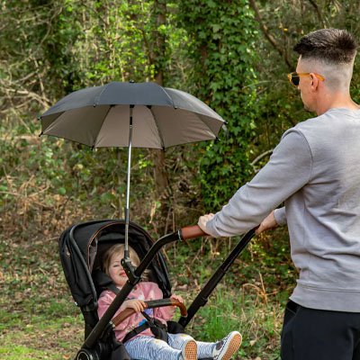 Papa en promenade avec son bébé dans une poussette munie d'une ombrelle beige pour se protéger du soleil.