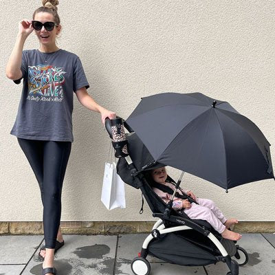 Maman marchant en ville avec son bébé dans une poussette équipée d'une ombrelle noire de protection solaire