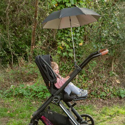 Bébé en promenade dans la nature. Confortablement installé dans une poussette avec ombrelle argentée 