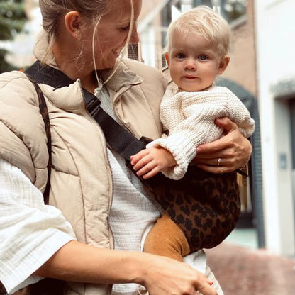 Maman souriante portant son bébé avec une écharpe bébé motif léopard pendant une promenade automnale.