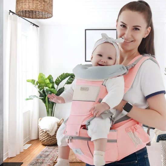 Maman souriante avec son bébé dans un pote-bébé ergonomique rose, parfait pour les promenades et la maison.