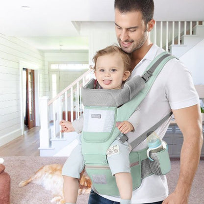 Papa portant son bébé dans un porte-bébé ergonomique vert à la maison, confort et sécurité pour les sorties.