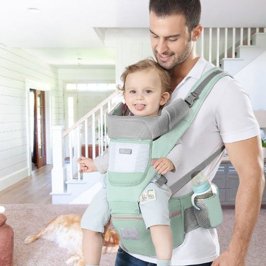 Papa portant son bébé dans un porte-bébé ergonomique vert à la maison, confort et sécurité pour les sorties.