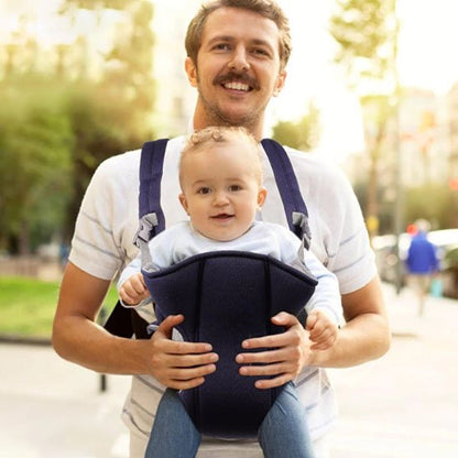 Papa souriant portant son bébé dans un porte-bébé noir pendant une promenade au parc.