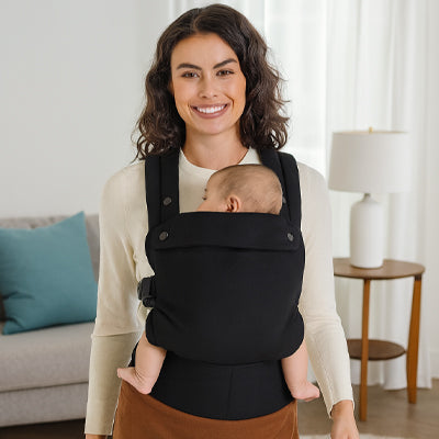 Porte bébé physiologique noir assurant un confort optimal pour maman et bébé à la maison.