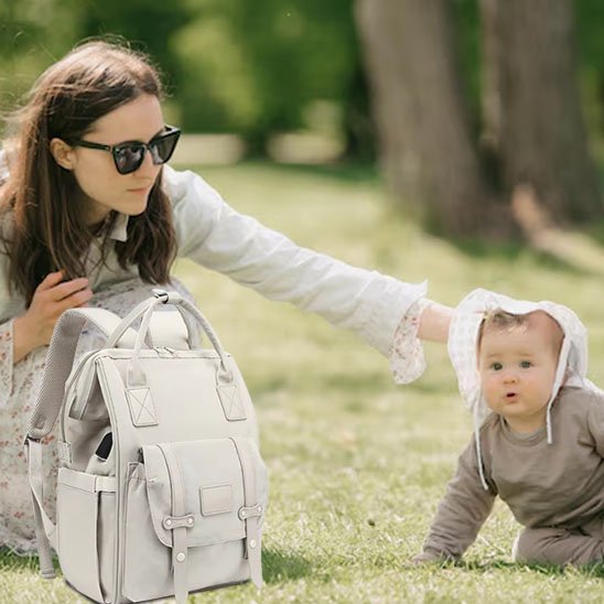 Maman assise dans l'herbe avec son bébé et un sac à langer beige