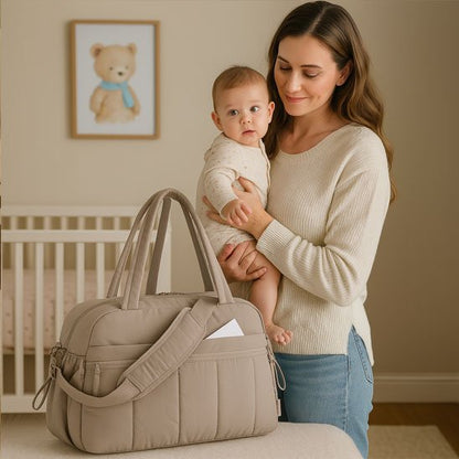 Sac à langer gris avec multiples poches à côté d'une maman tenant son bébé